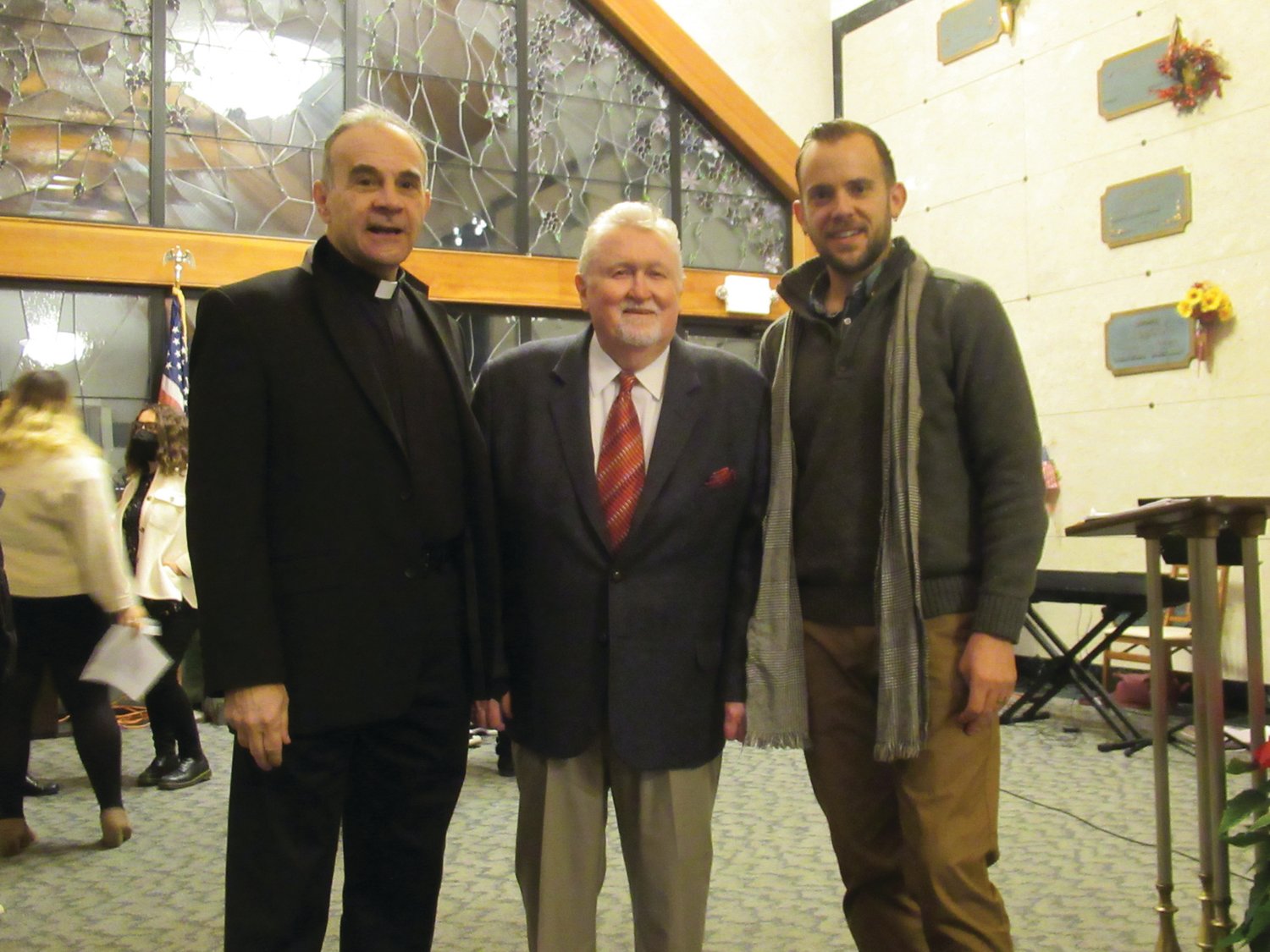 LINKED LEADERS: Joseph Swift (center), president of Highland Memorial Park Cemetery and the Johnston Lions Club, is joined by Rev. Father Albert Ranallo of St. Ann’s  Church in Providence and Matt Gingras, Director of the JHS Concert Chorus, during Sunday’s special Christmas Remembrance Ceremony.